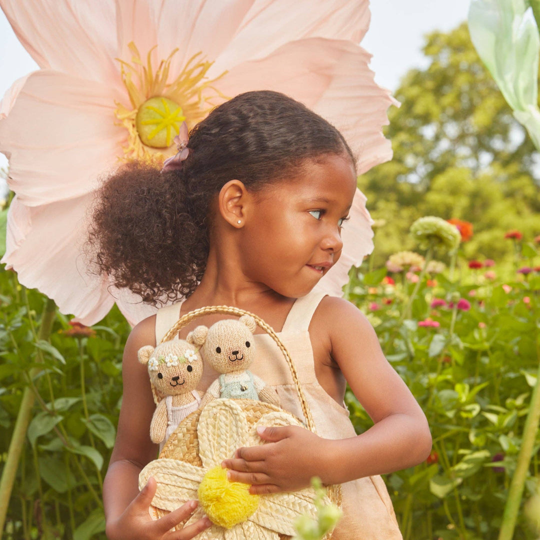 Young girl in a garden holding teddy bears and a straw hat, with a large flower.