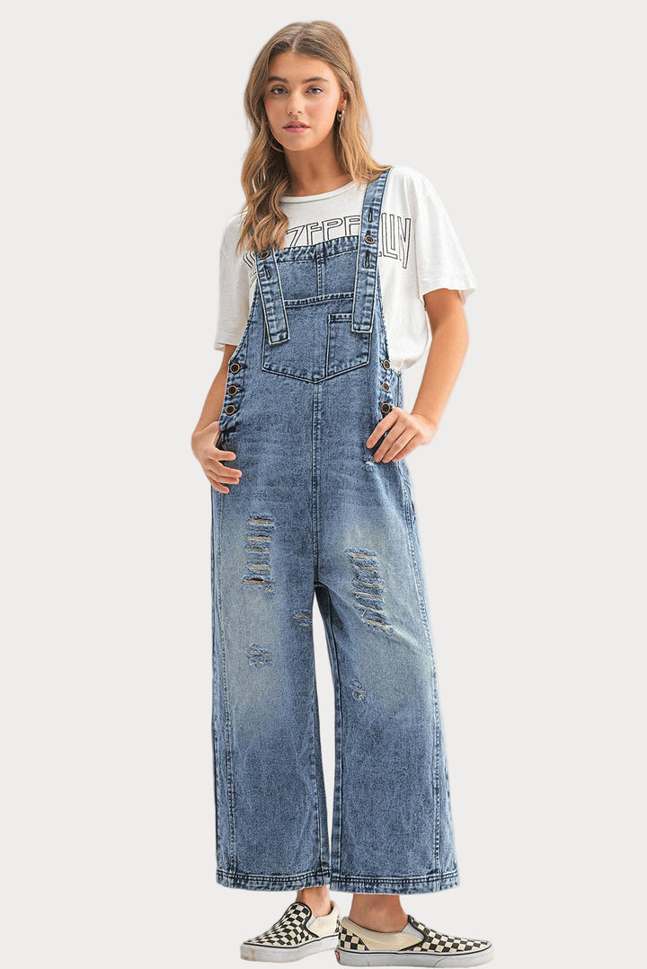Woman wearing blue distressed denim overalls on a white background