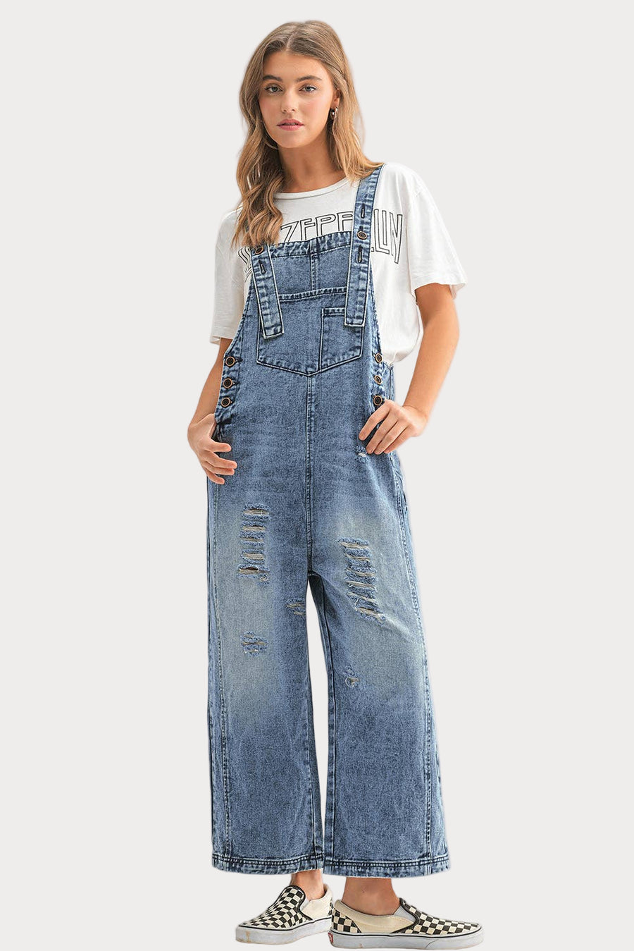 Woman wearing blue distressed denim overalls on a white background