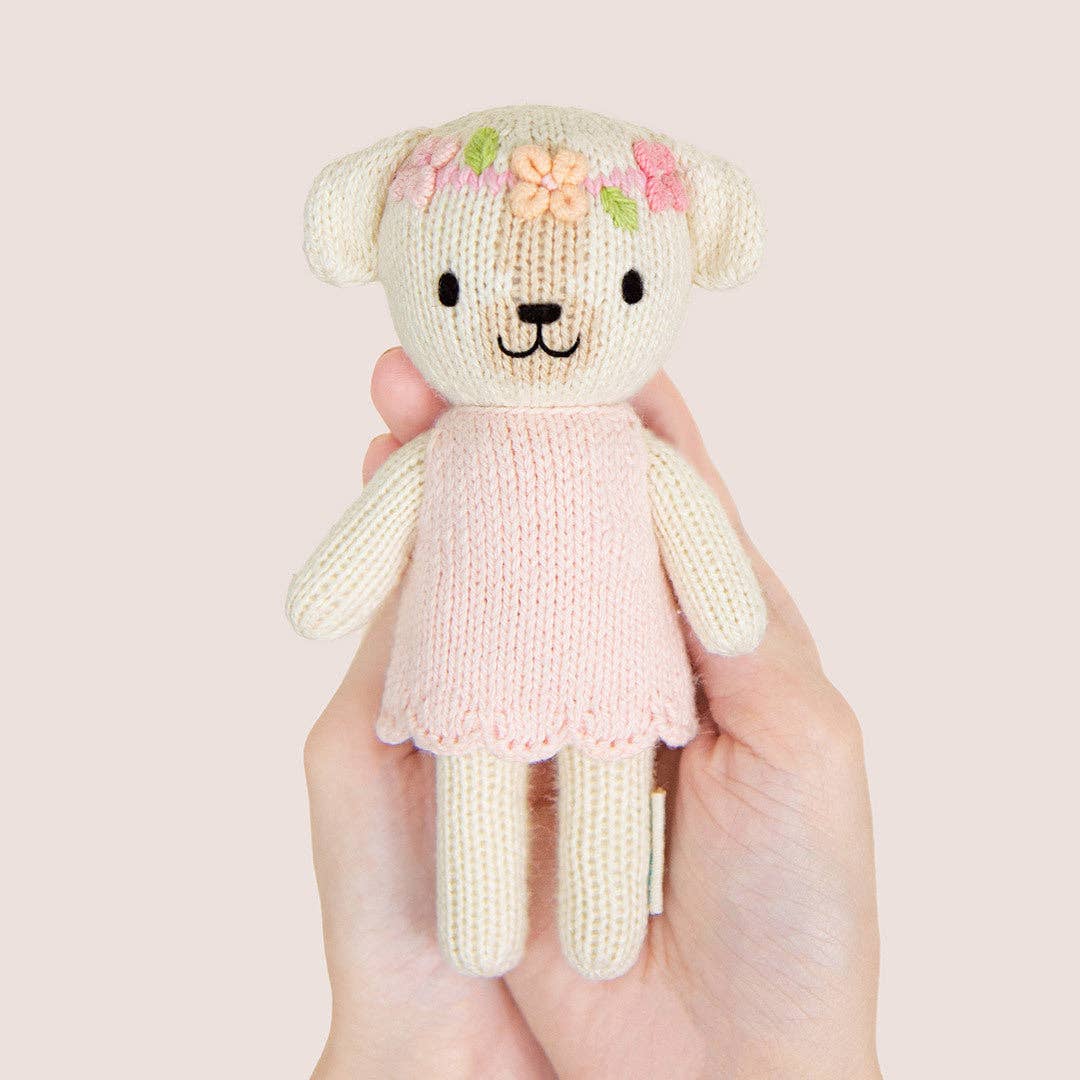 Knitted dog with a pink dress held in hands against a light background