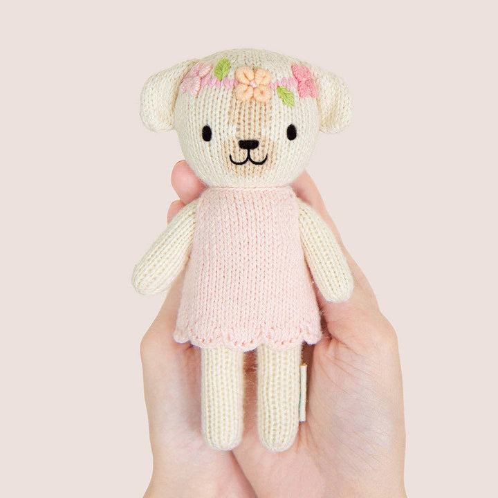 Knitted dog with a pink dress held in hands against a light background