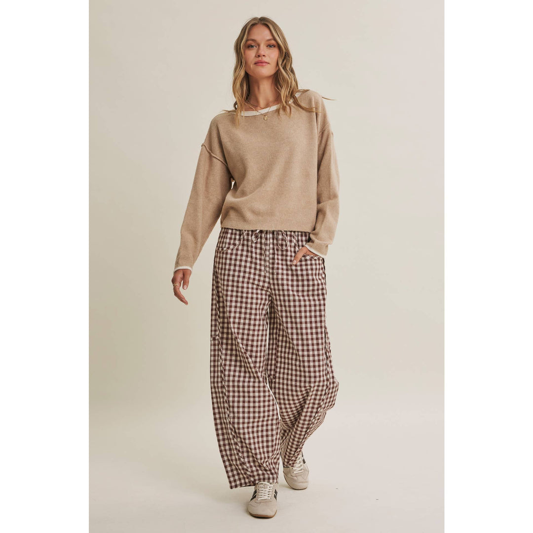 Woman wearing a beige sweater and plaid pants on a plain background