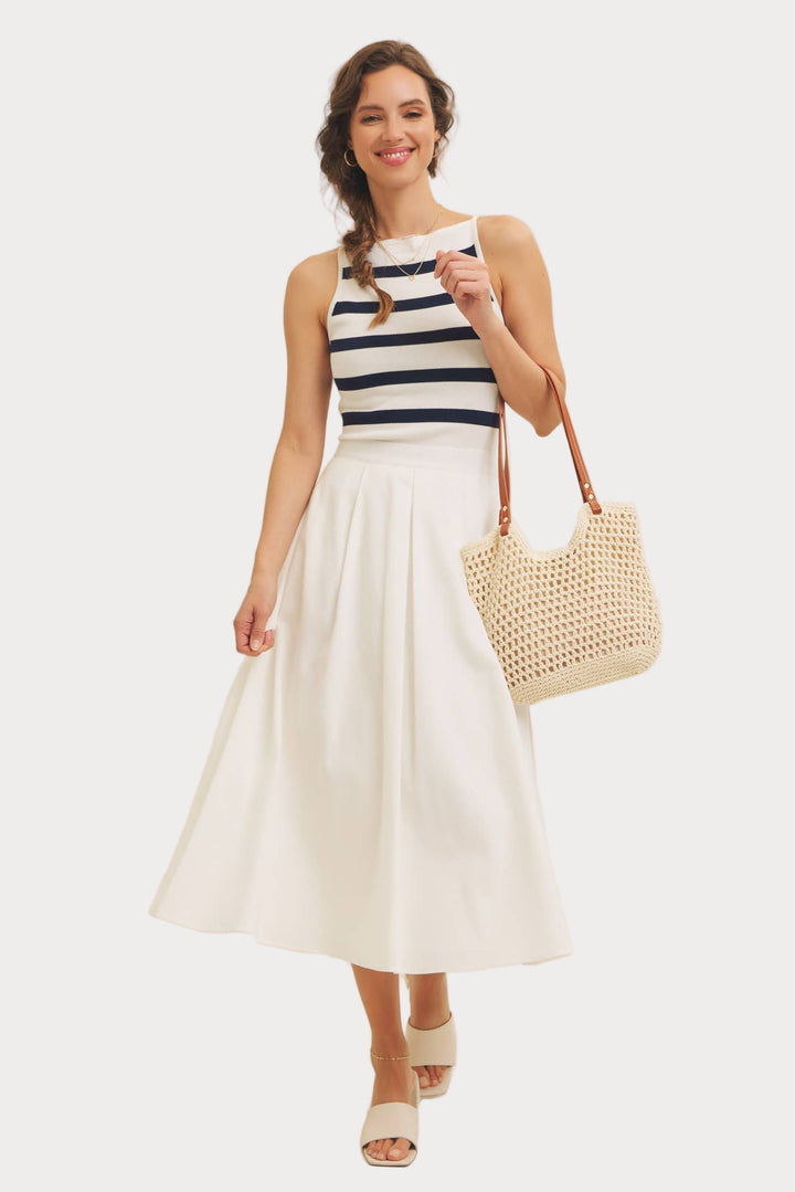 A woman wearing a striped sweater tank top with white lower attire, accessorized with a light-colored handbag and footwear.
