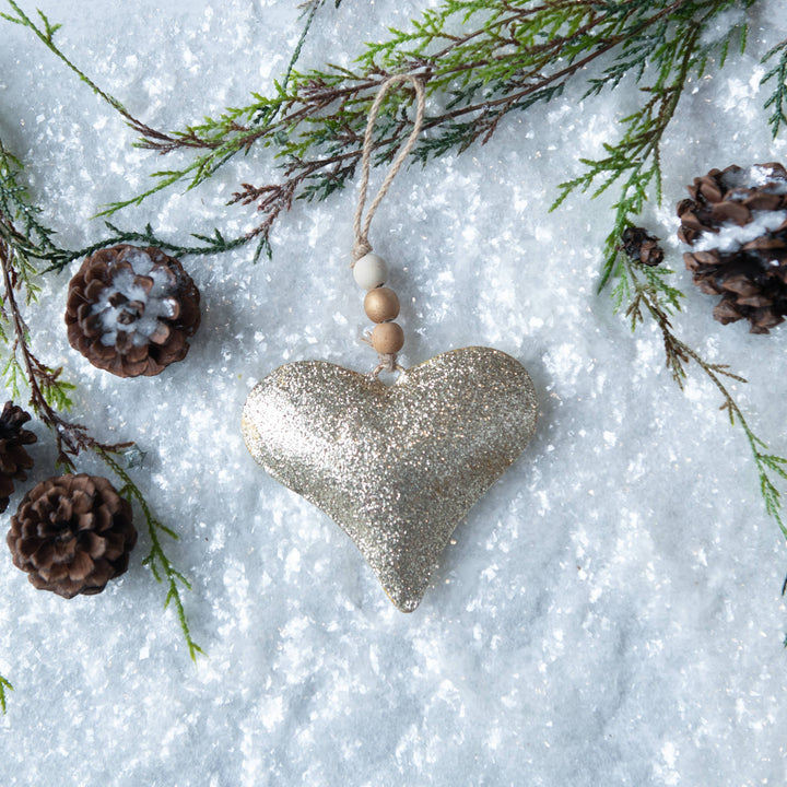 gold metal heart ornament with twine and wood beads on snowy background
