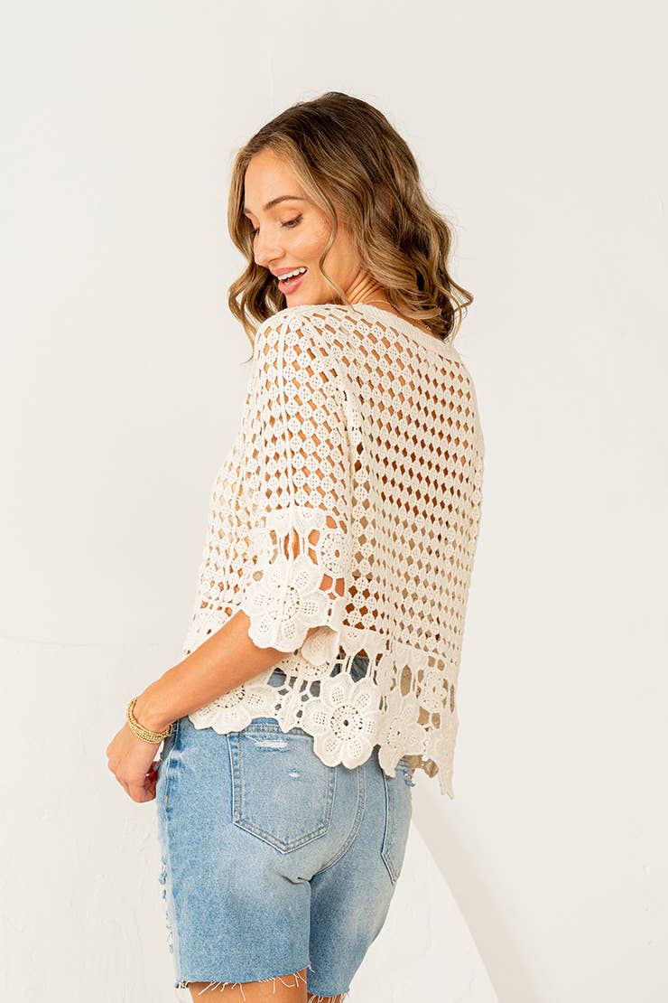 Woman wearing cream crochet button-down top with scalloped lace hem and distressed denim shorts