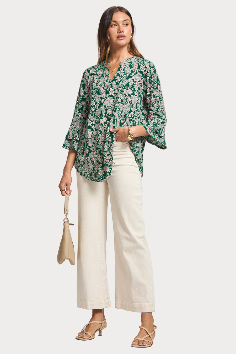 Woman wearing a green floral blouse and white pants on a white background