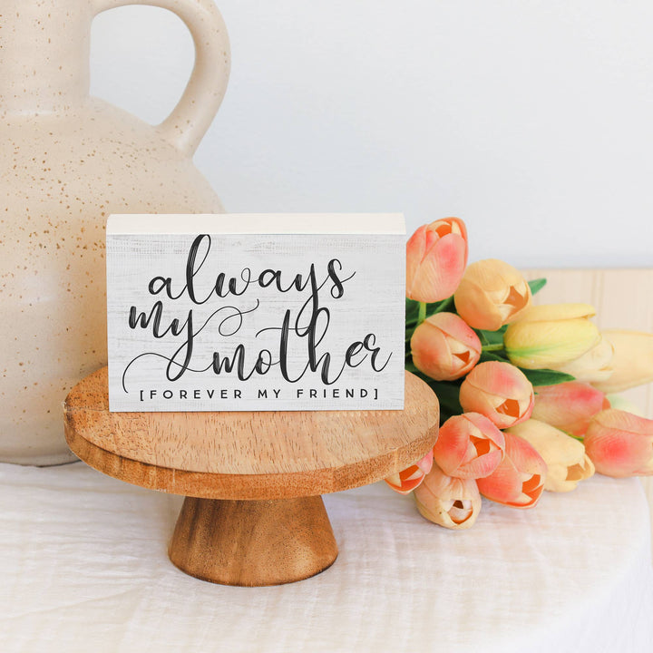 Block sign with 'always my mother, forever my friend' text on a wooden stand with tulips.