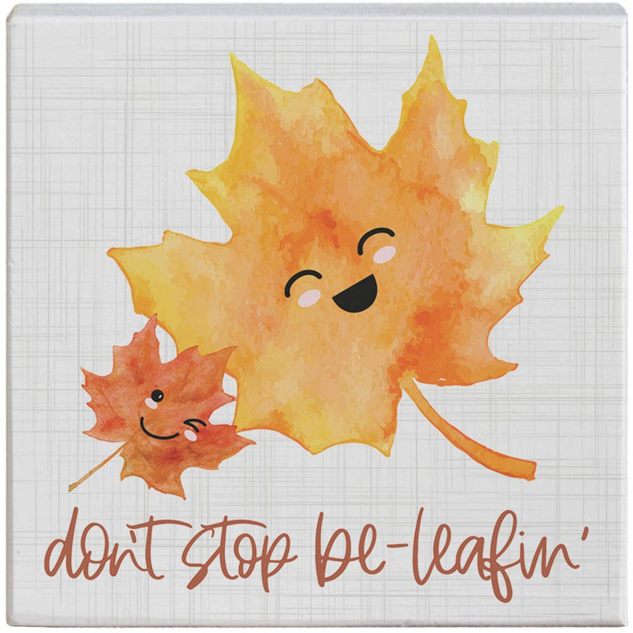 Two smiling autumn leaves with a face and the text 'don't stop be-leafin'' on a white background.