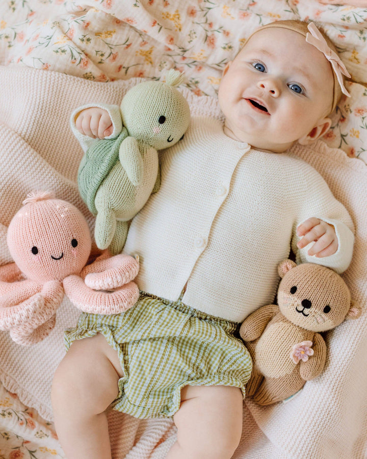 Baby lying on a floral blanket with soft  knitted toys