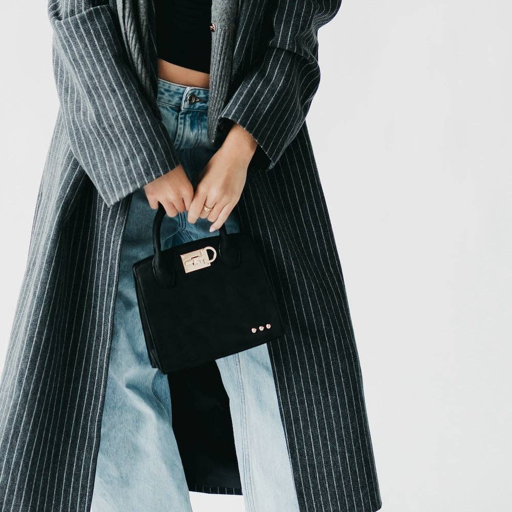 Person wearing a long pinstripe coat holding a black handbag against a plain background