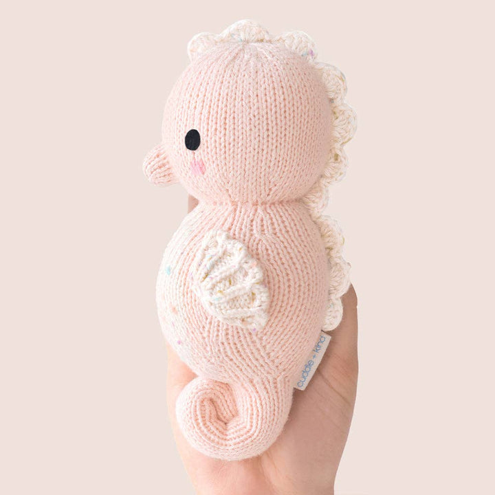 Knitted pink seahorse toy held by a hand against a light background
