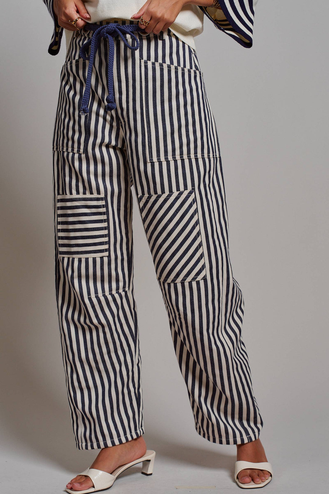 Woman wearing navy and ivory railroad stripe utility pants with oversized patch pockets, braided drawstring waist, and relaxed straight-leg fit.