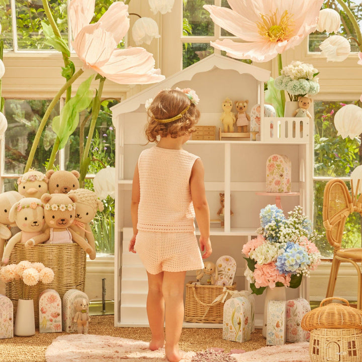 Child in a beige short set standing in a playroom with knit toys and flowers
