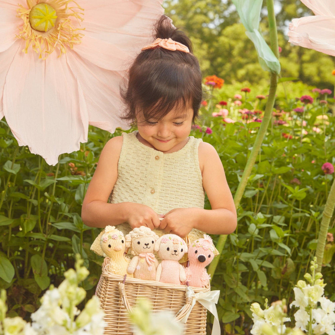 Young girl holding a basket of knit animals in a garden setting with large flowers.