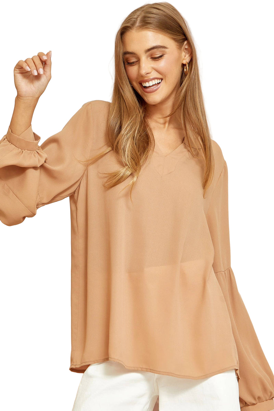A female model wearing a beige split neck long sleeve top with a loose fit, paired with white pants.