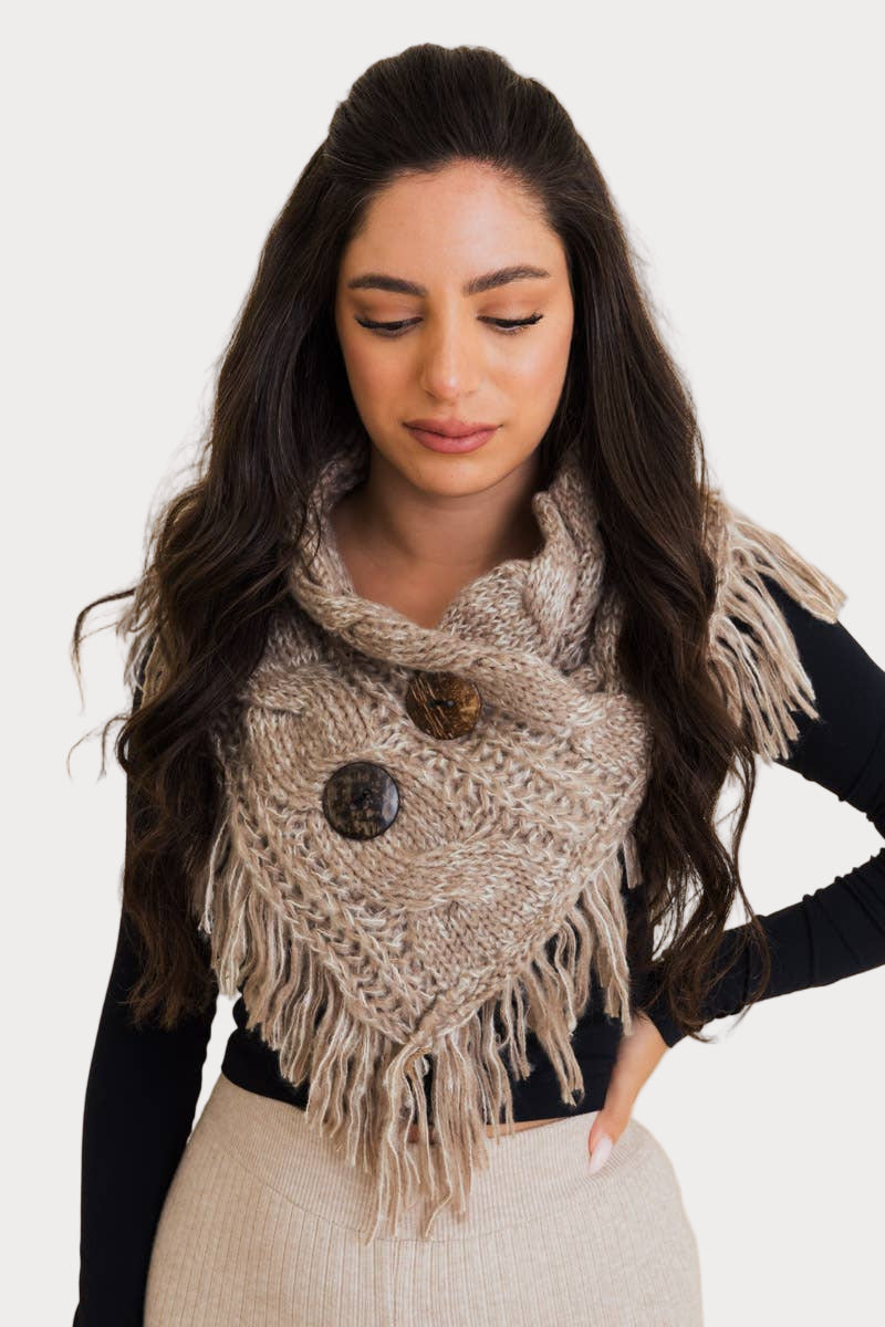 Woman wearing a heathered knit shoulder warmer with fringe and large coco buttons in neutral beige tones.