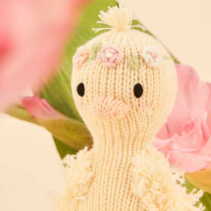 Knitted duck toy with floral decorations on a soft focus background