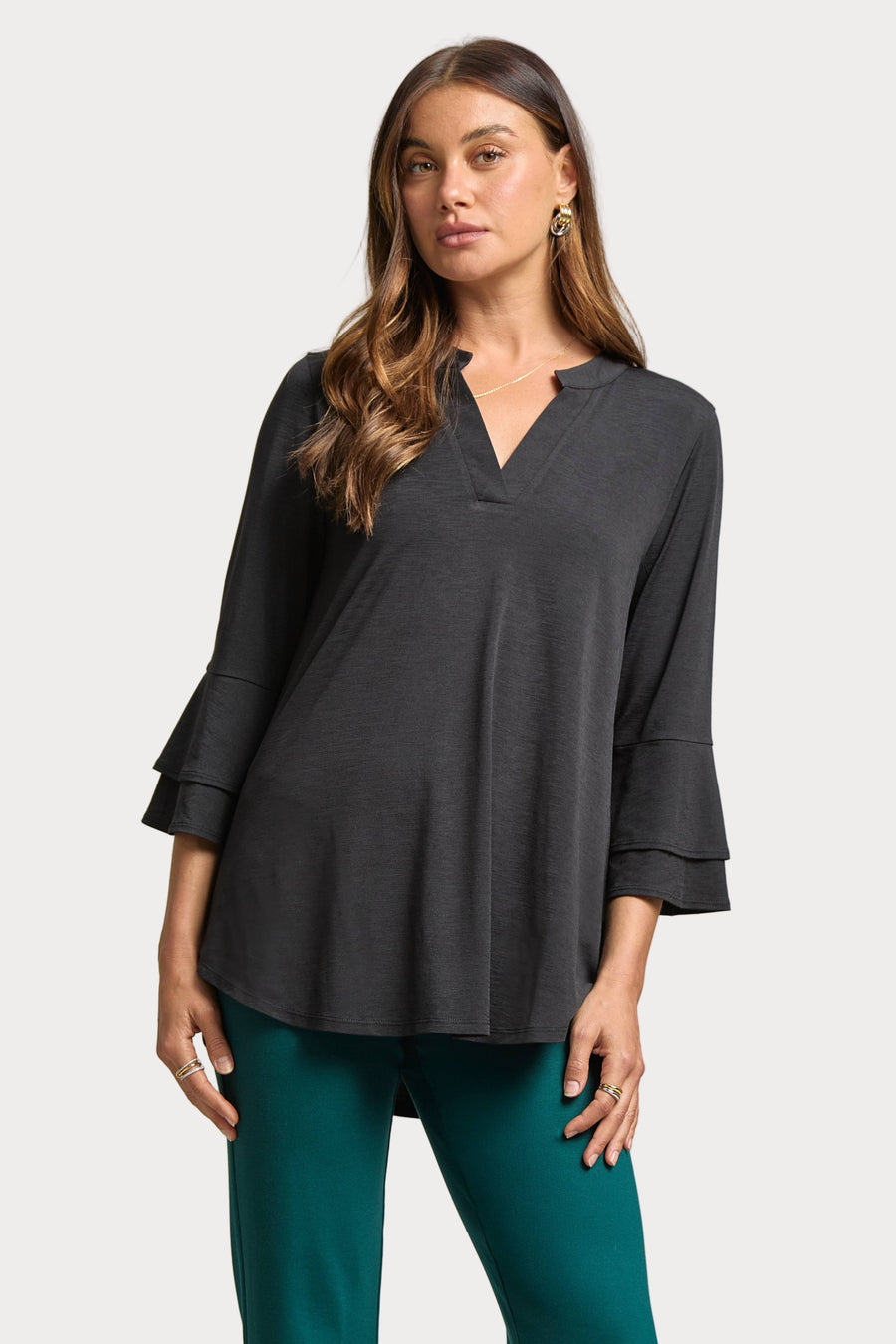 Woman wearing a dark gray blouse and teal pants on a plain background