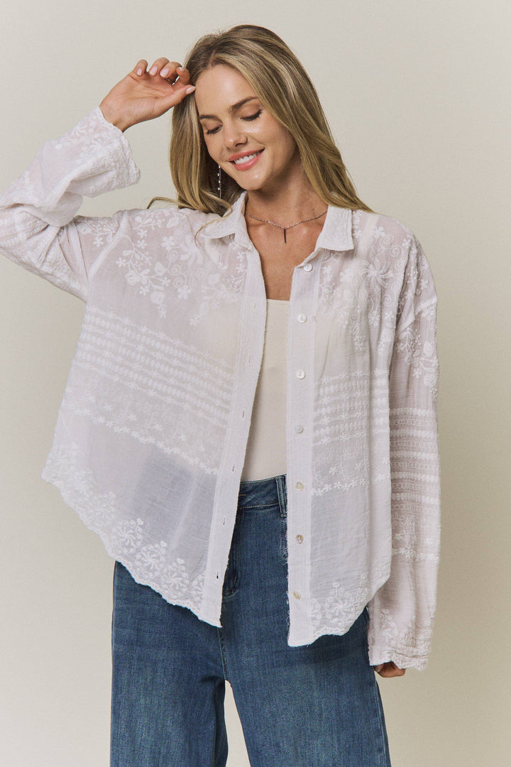 Woman wearing a light-colored lace embroidered blouse and blue jeans against a plain background
