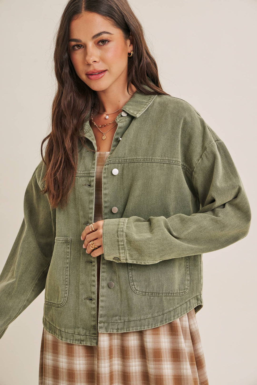 Woman wearing a olive green jacket over a plaid dress on a beige background