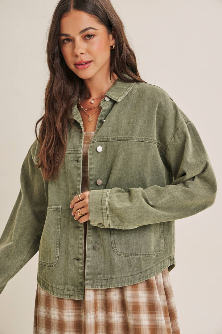Woman wearing a olive green jacket over a plaid dress on a beige background