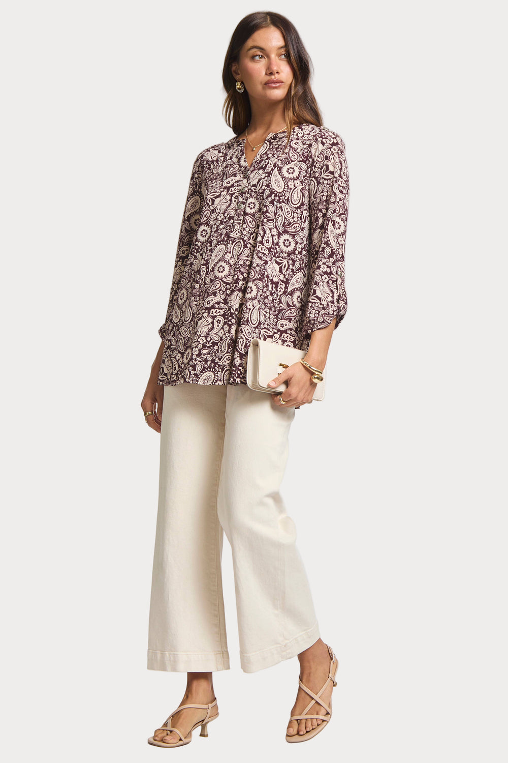 Woman wearing a patterned blouse and white pants on a plain background