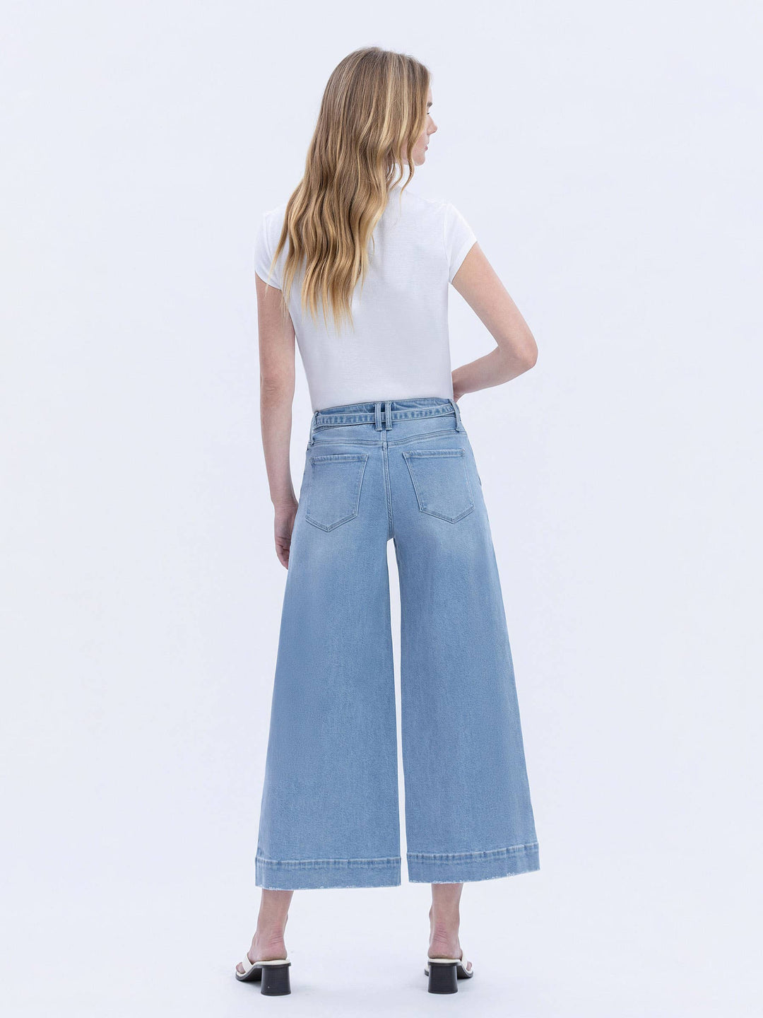 Woman wearing light blue wide-leg jeans and a white top on a white background