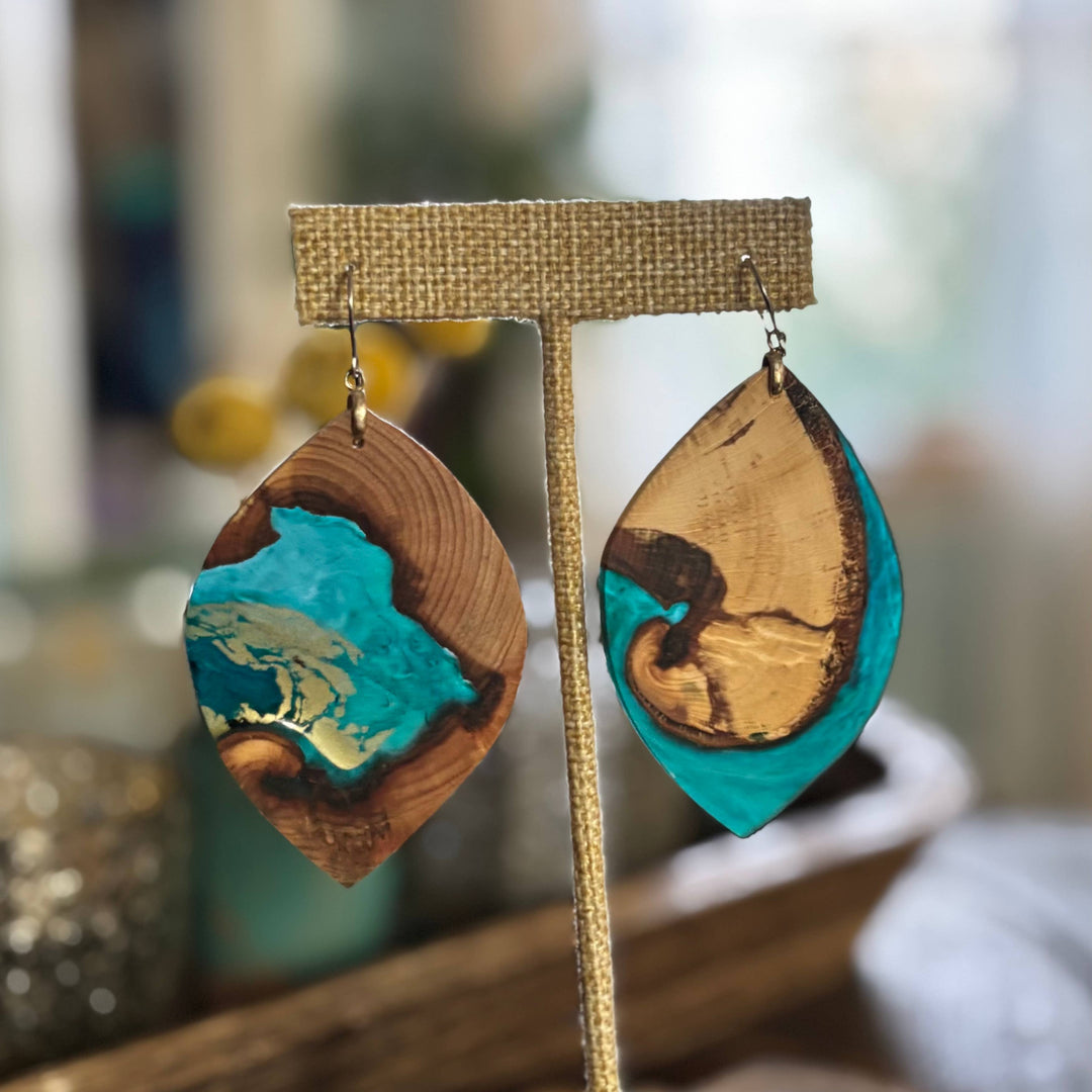Wooden earrings with turquoise and gold accents on a stand against a blurred background