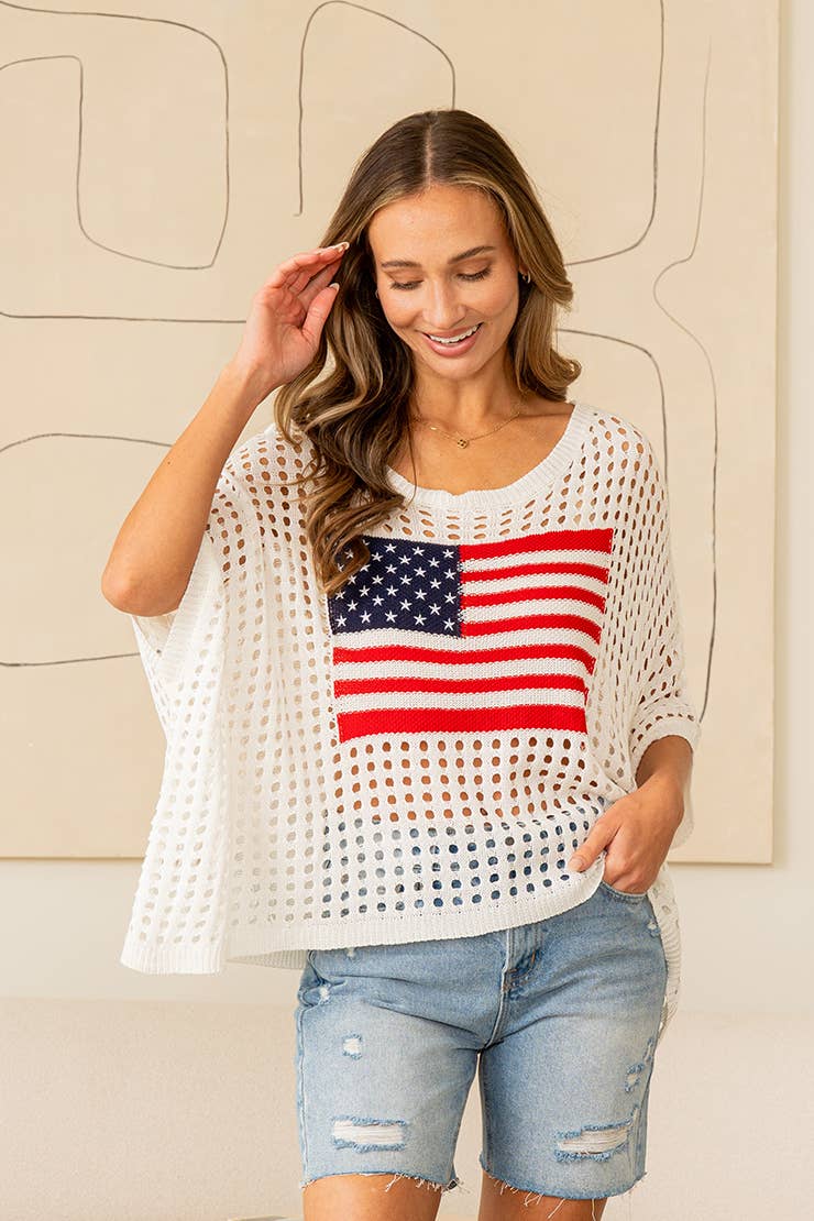 Woman wearing white open-knit sweater top with American flag design and denim jeans