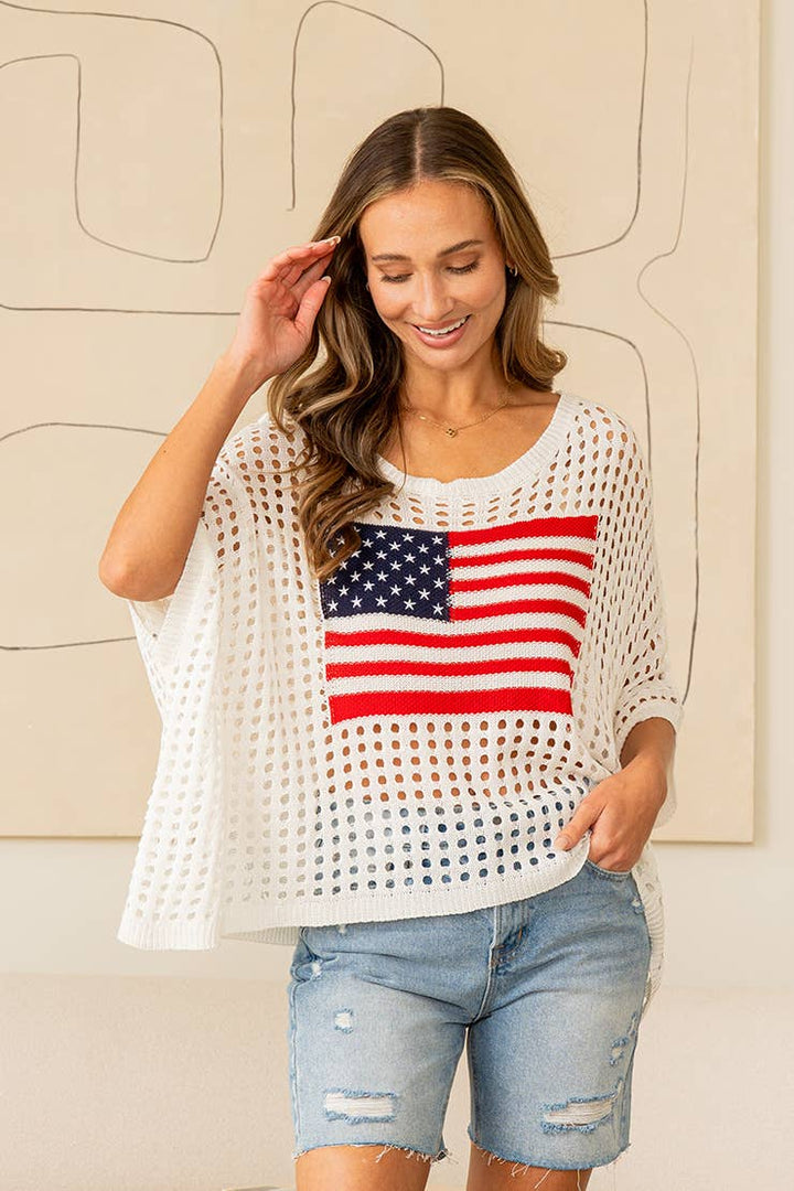 Woman wearing white open-knit sweater top with American flag design and denim jeans