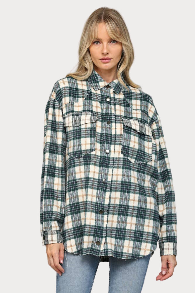 A woman wearing an oversized hunter green, cream, and tan plaid shacket with raw edge chest pockets and snap buttons, paired with light wash jeans.

