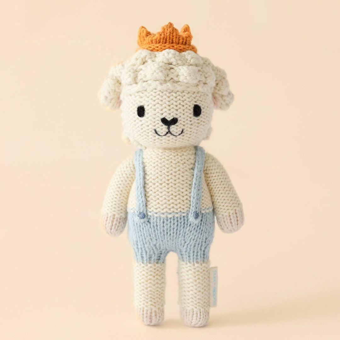 Knitted toy lamb with a crown and overalls on a beige background