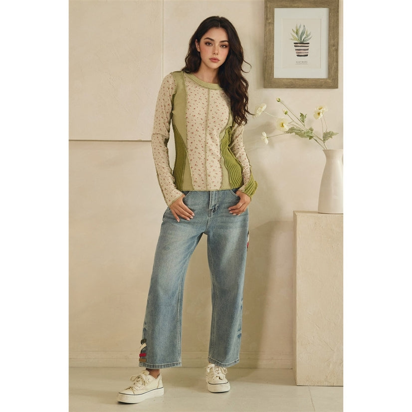 Woman wearing a green patterned top and blue jeans standing in a room with a neutral color scheme.
