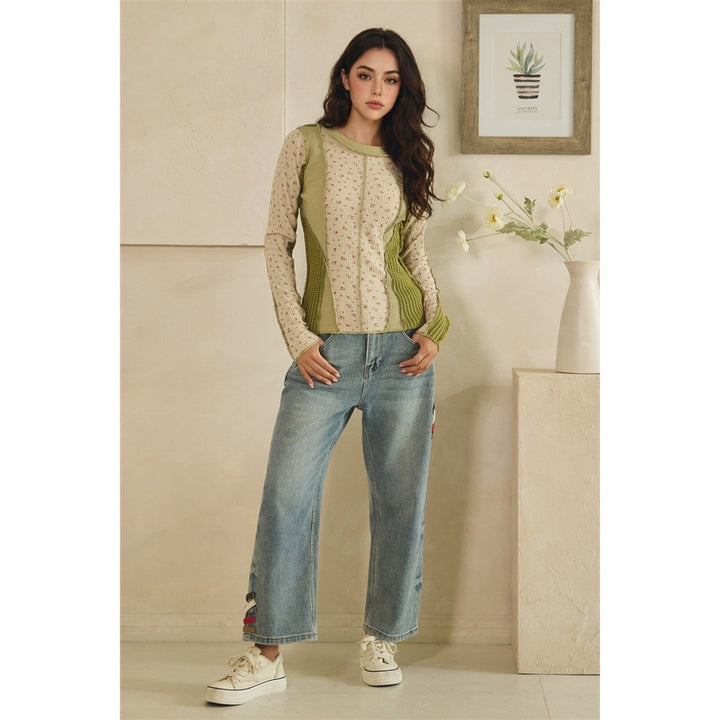 Woman wearing a green patterned top and blue jeans standing in a room with a neutral color scheme.