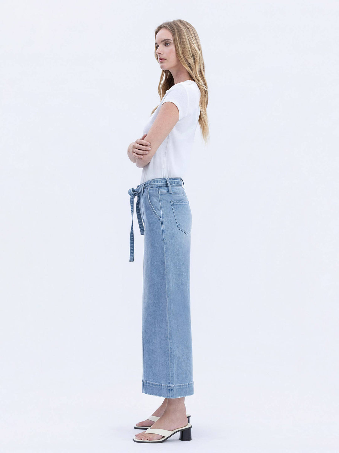 Woman wearing a white t-shirt and light blue jeans with a belt on a white background