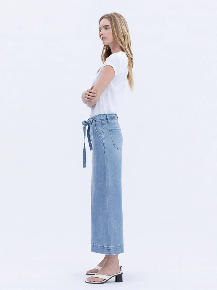 Woman wearing a white t-shirt and light blue jeans with a belt on a white background