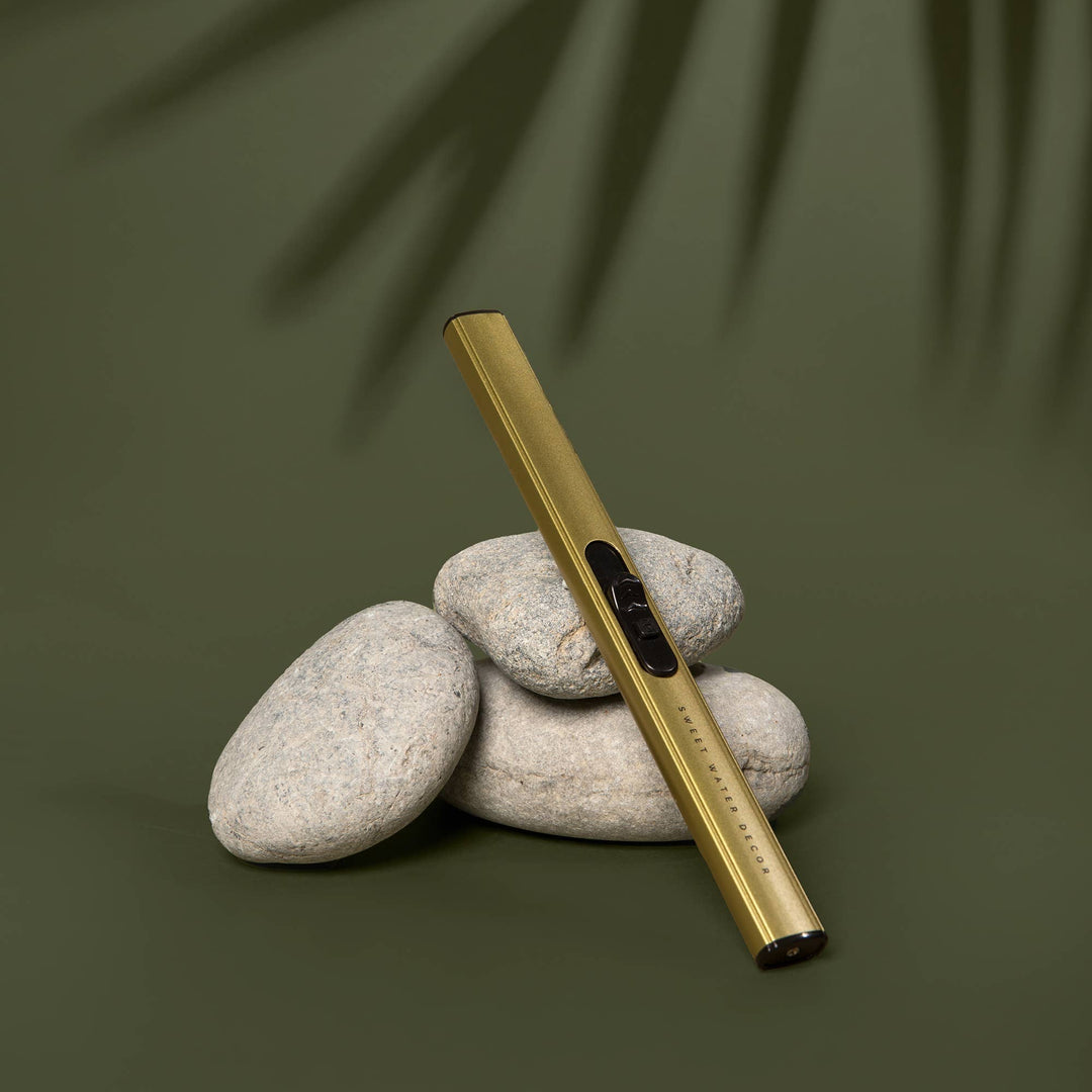 Gold electric lighter on stacked stones with a green leafy background