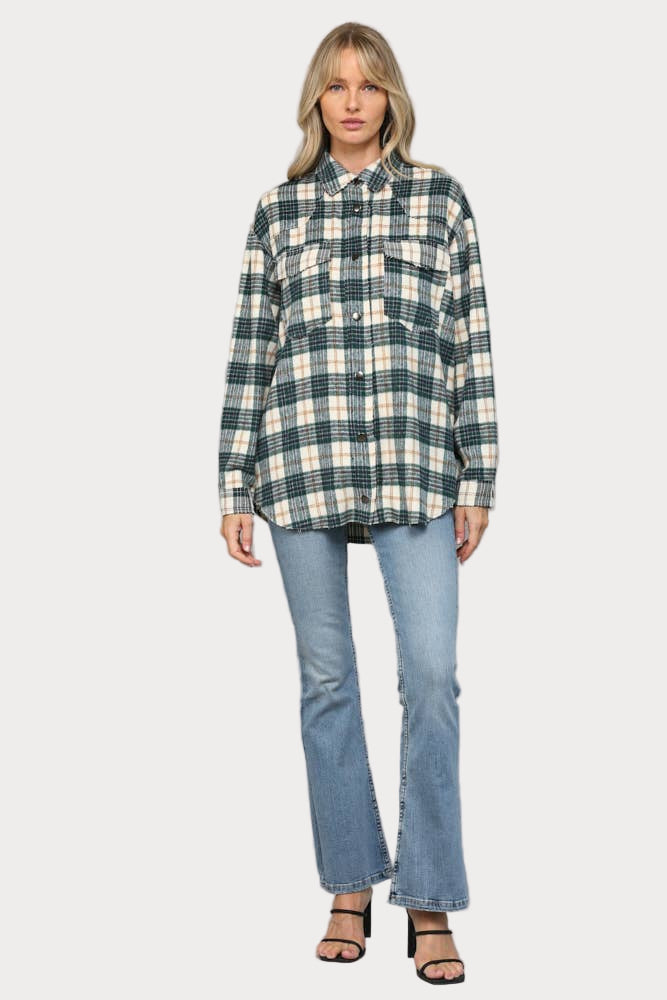 A woman wearing an oversized hunter green, cream, and tan plaid shacket with raw edge chest pockets and snap buttons, paired with light wash jeans.

