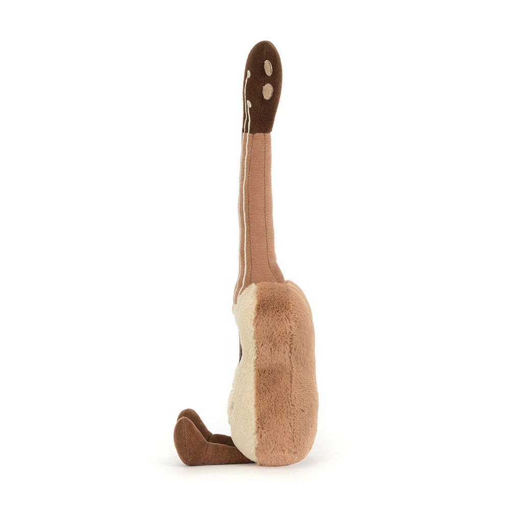 Side view of the Jellycat Amuseables Ukulele plush toy, showing its light beige body, dark brown neck, and corduroy brown feet extended forward on a white background.