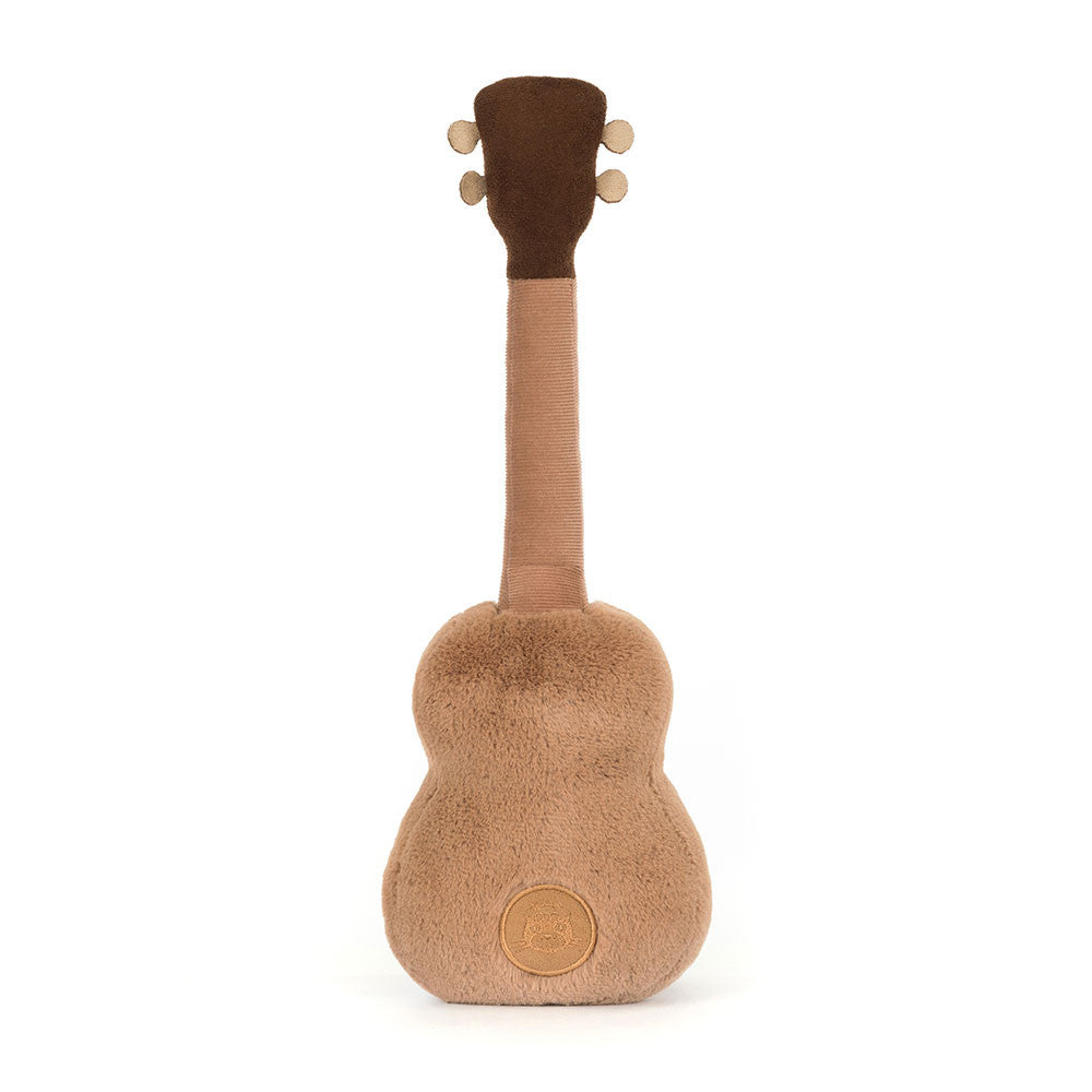 Back view of the Jellycat Amuseables Ukulele plush toy, showcasing its light brown textured back, dark brown headstock, and a round brown Jellycat brand tag stitched on the lower back, on a white background.