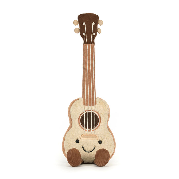 A soft, plush Jellycat Amuseables Ukulele toy with a light beige body, dark brown neck and headstock, embroidered black eyes and a smiling mouth, a brown soundhole, and white 'strings,' sitting with two corduroy brown feet extended forward on a white background.