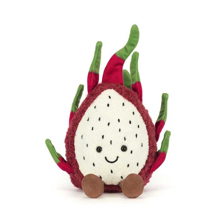 Front view of the Jellycat Amuseables Dragon Fruit plush, showcasing its textured deep fuchsia rind, a soft cream-colored 'flesh' section with embroidered black seeds and a happy face, and green and fuchsia spiky leaves, with two brown corduroy feet extending forward."