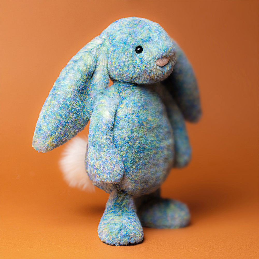Bashful Luxe Bunny Azure standing  showing off her luxe coat of multicolored fur , fluffy tail and her soft chunky paws.
shown on a orange background.