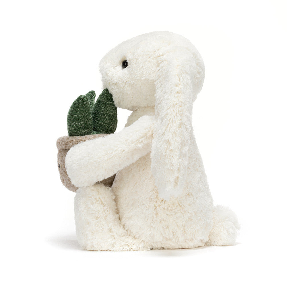 Cream plush bunny holding a smiling potted plant with green leaves. Facing left side profile
