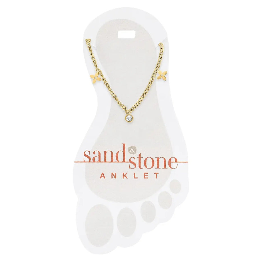 gold stainless steel anklet with clover accents and cz dangle charm a white display card with 'sand & stone' branding.