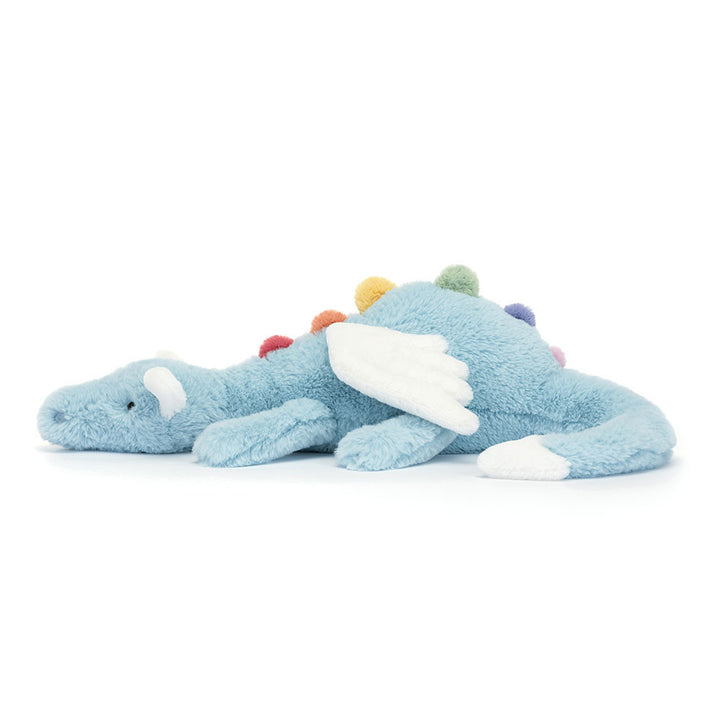 Jellycat Sky Dragon plush with soft blue fur, white wings, and pastel accents lying on a white background side view