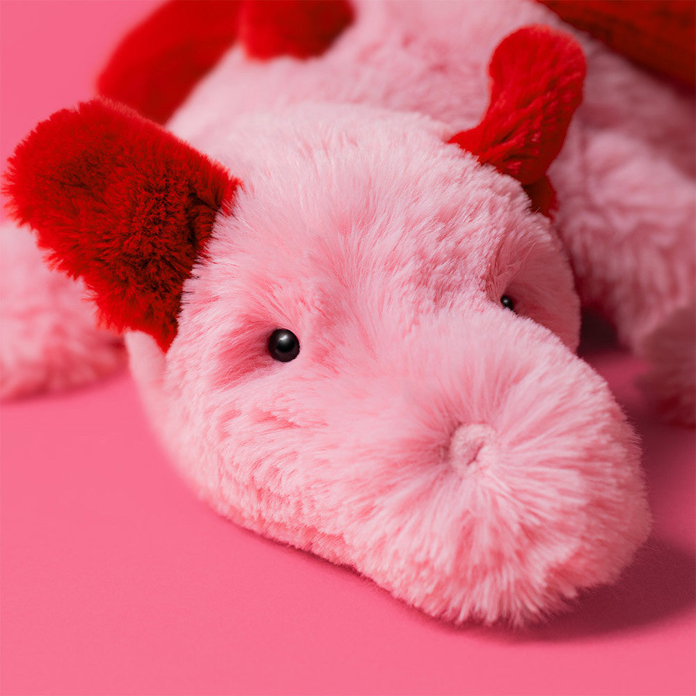 closeup face details Jellycat Heart Dragon plush with soft pink fur, red heart accents, and a cuddly dragon design on a pinkbackground