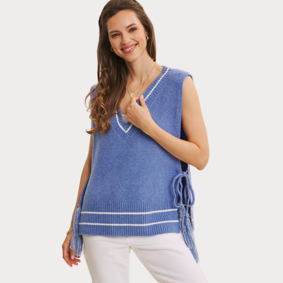 Woman wearing a blue side-tie sweater vest with V-neckline, styled with white pants.