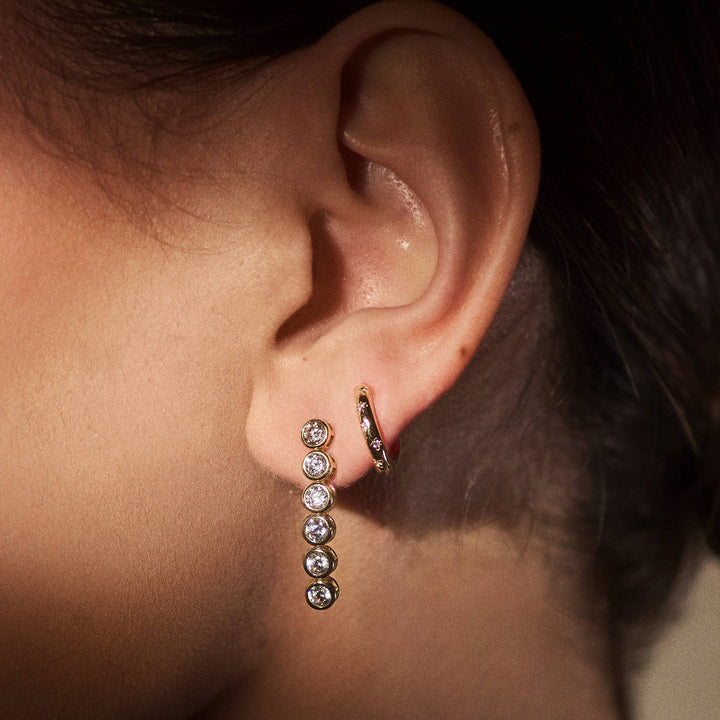 Close-up of an ear wearing a dangling earring and a hoop earring.