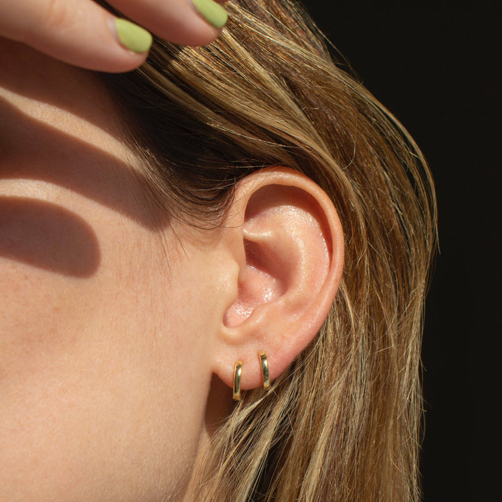 Close-up of an ear with gold hoop earrings against a dark background